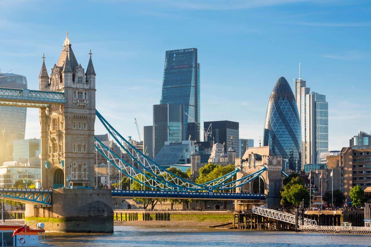 London skyline featuring the Tower Bridge, the Gherkin building, and modern skyscrapers at sunset.