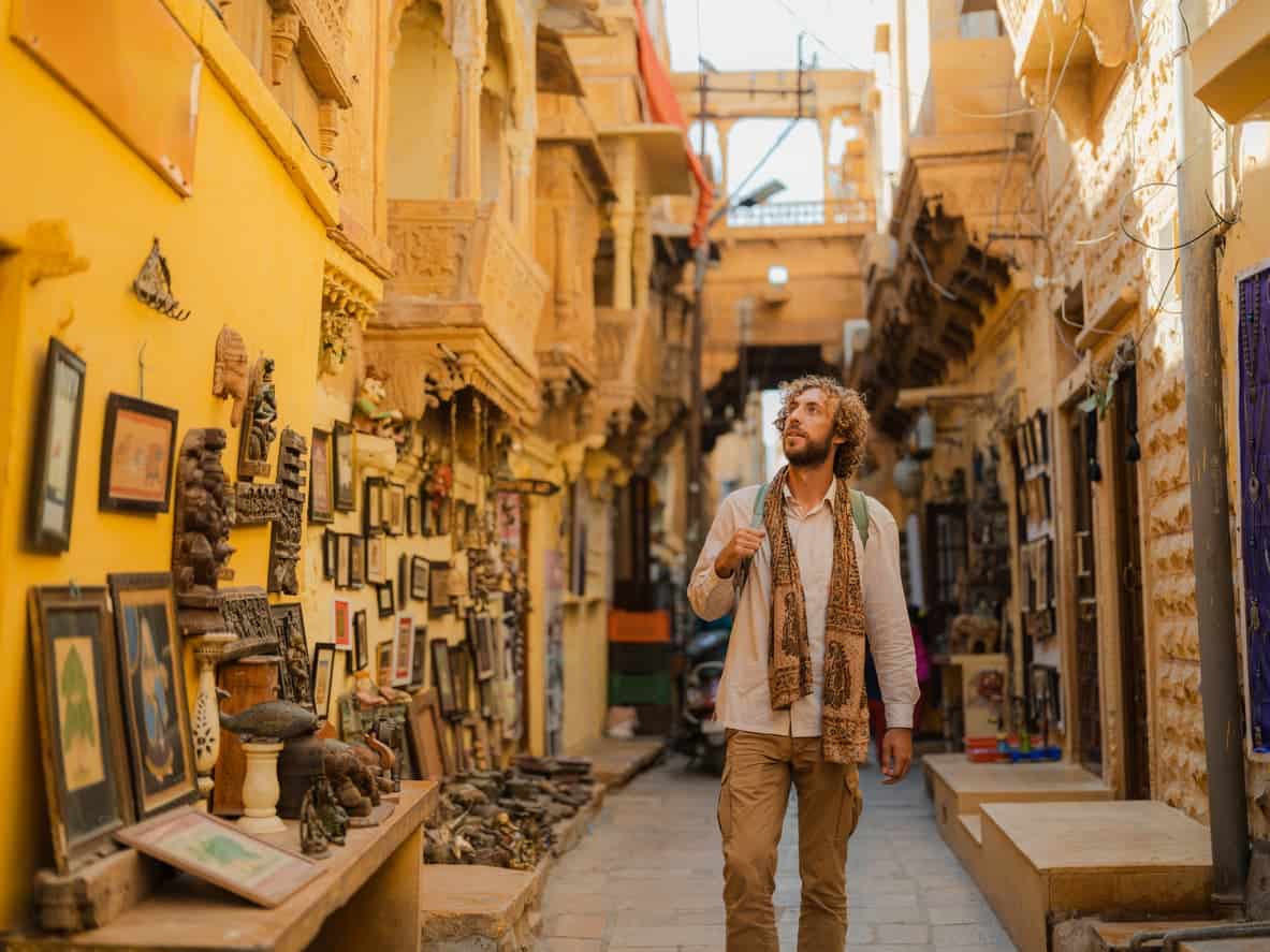 Traveler walking through a vibrant street market in India surrounded by traditional art and crafts