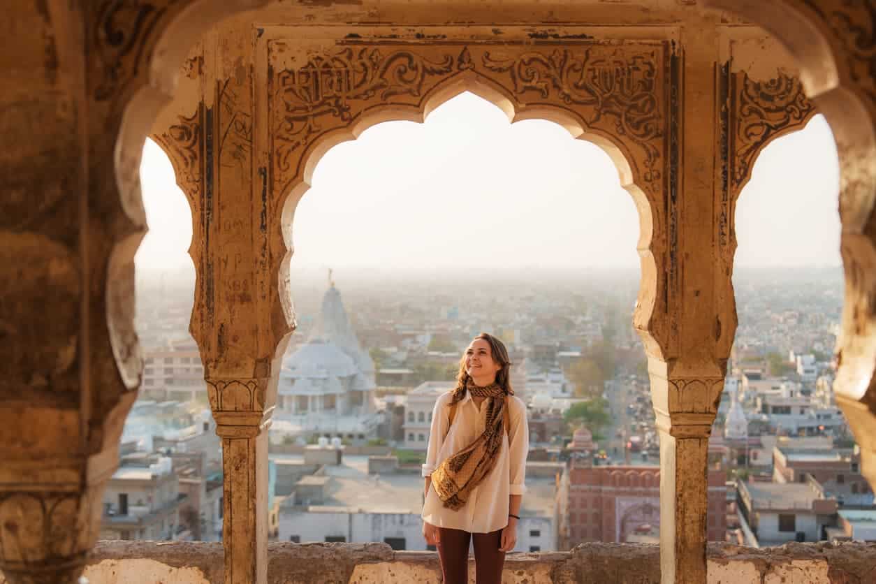 woman standing in an ancient Indian architectural archway overlooking a cityscape at sunset