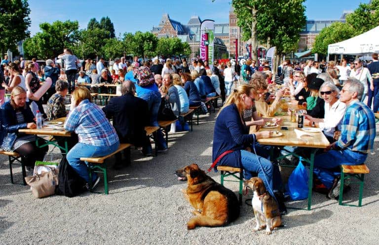 Amsterdam, The Netherlands - A large crowd of local people and tourists enjoy eating a meal served at very long tables in the Museumplein of Amsterdam.