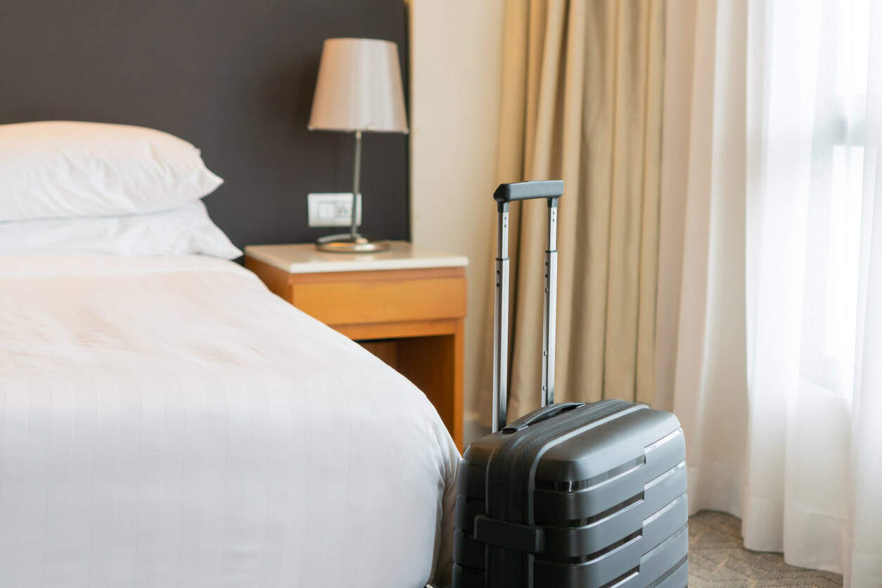 Carry-on suitcase standing next to a bed inside a modern hotel room