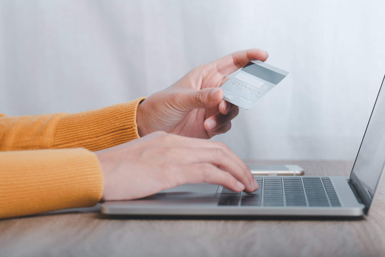 Person holding a credit card while typing on a laptop to book travel online