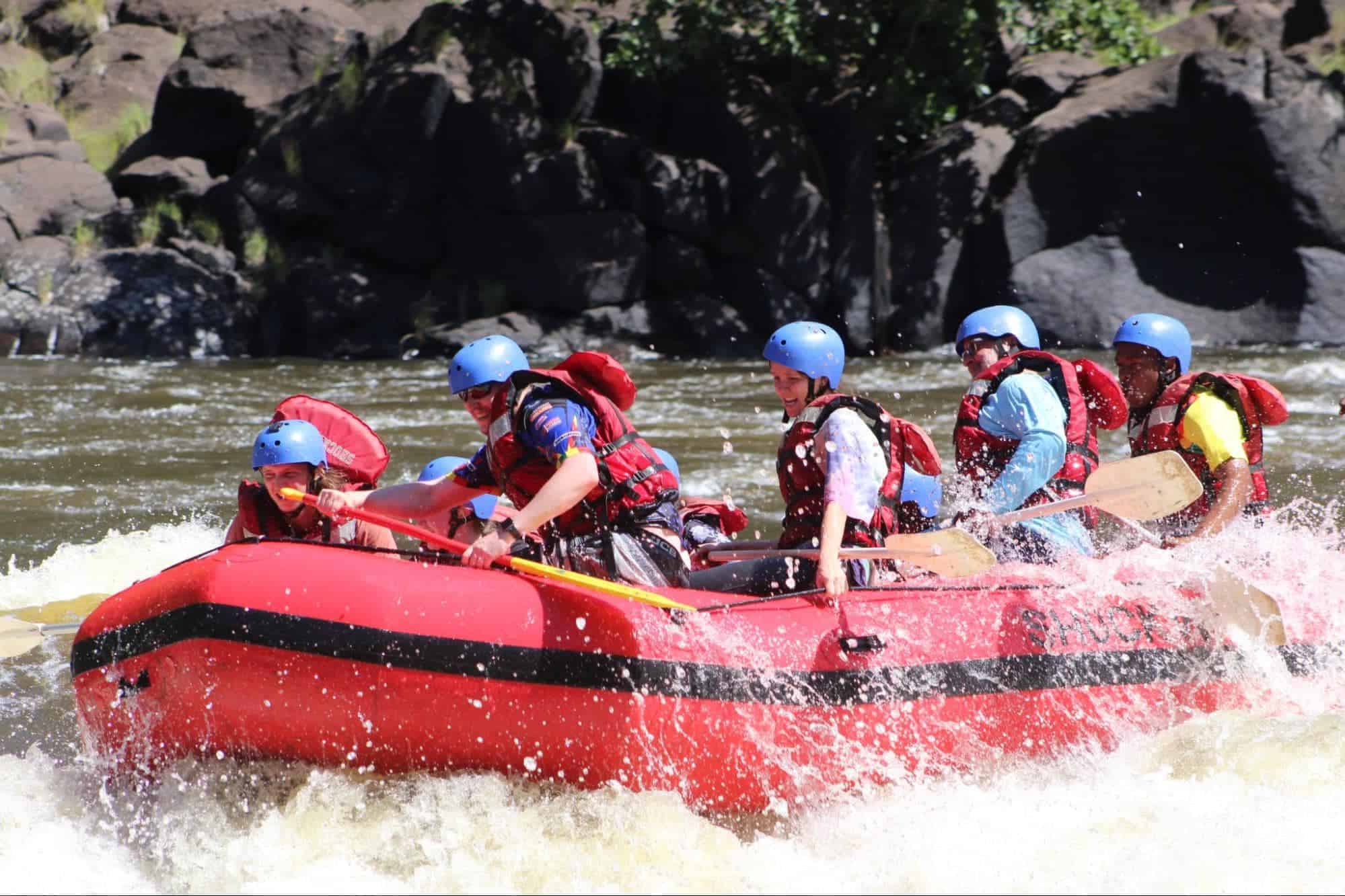 Group of people white water rafting through river rapids wearing helmets and life jackets during an outdoor adventure
