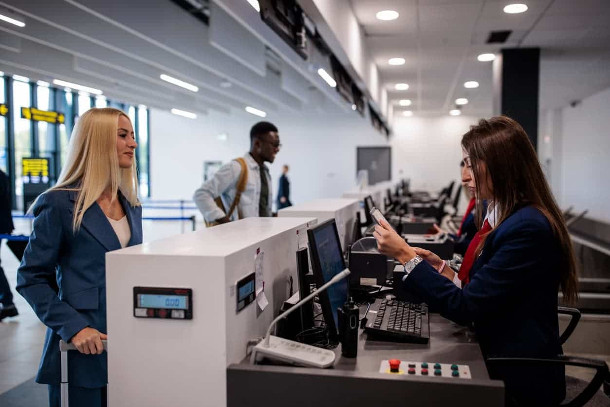 Airline passenger checking in at airport counter with staff reviewing ticket and travel documents