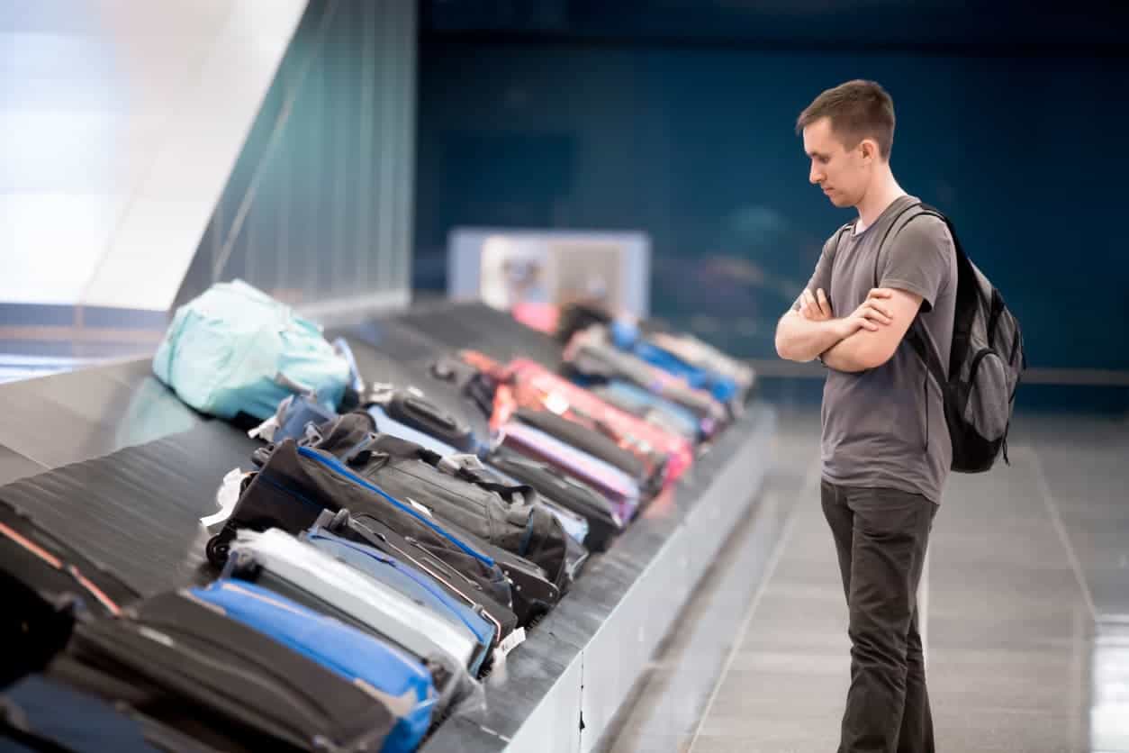 Passenger standing at baggage claim carousel waiting for luggage at airport