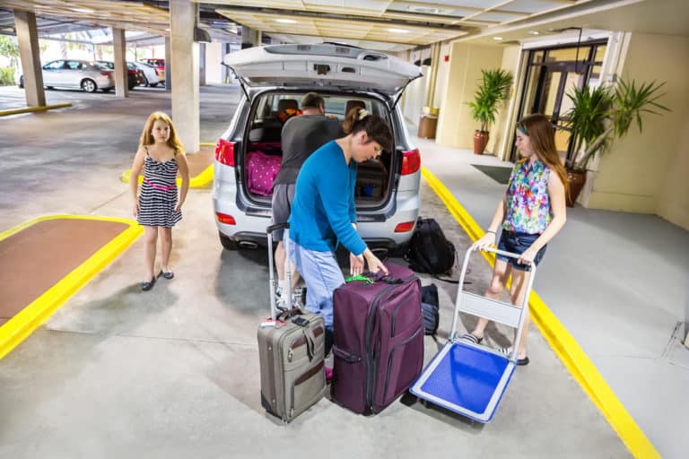 Family is putting their luggage in the car in preparation for leaving their hotel. RM