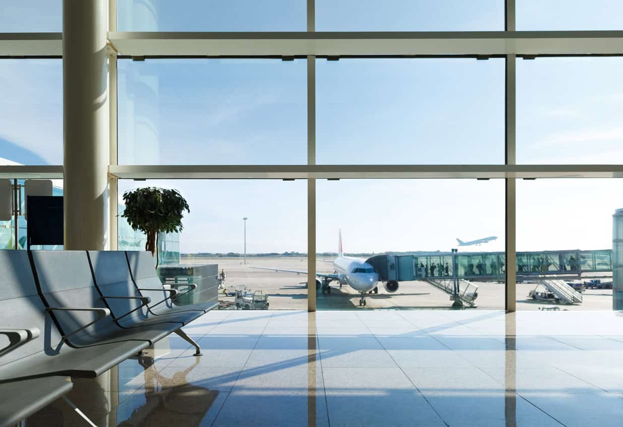 Airport terminal seating area with large windows overlooking airplane at the gate and passengers boarding through jet bridge