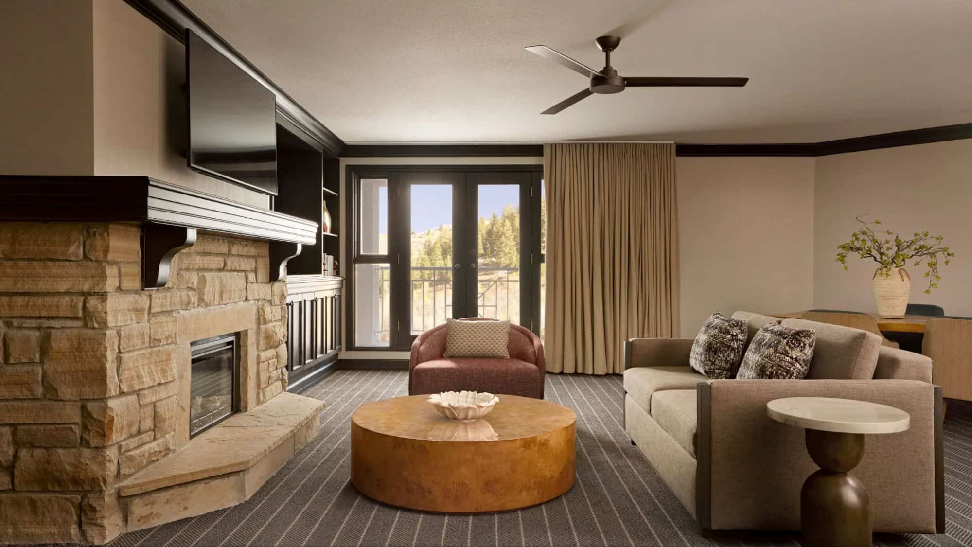 Spacious suite living room at Park Hyatt Beaver Creek Resort and Spa featuring a stone fireplace, modern seating area, ceiling fan, and balcony doors with mountain views