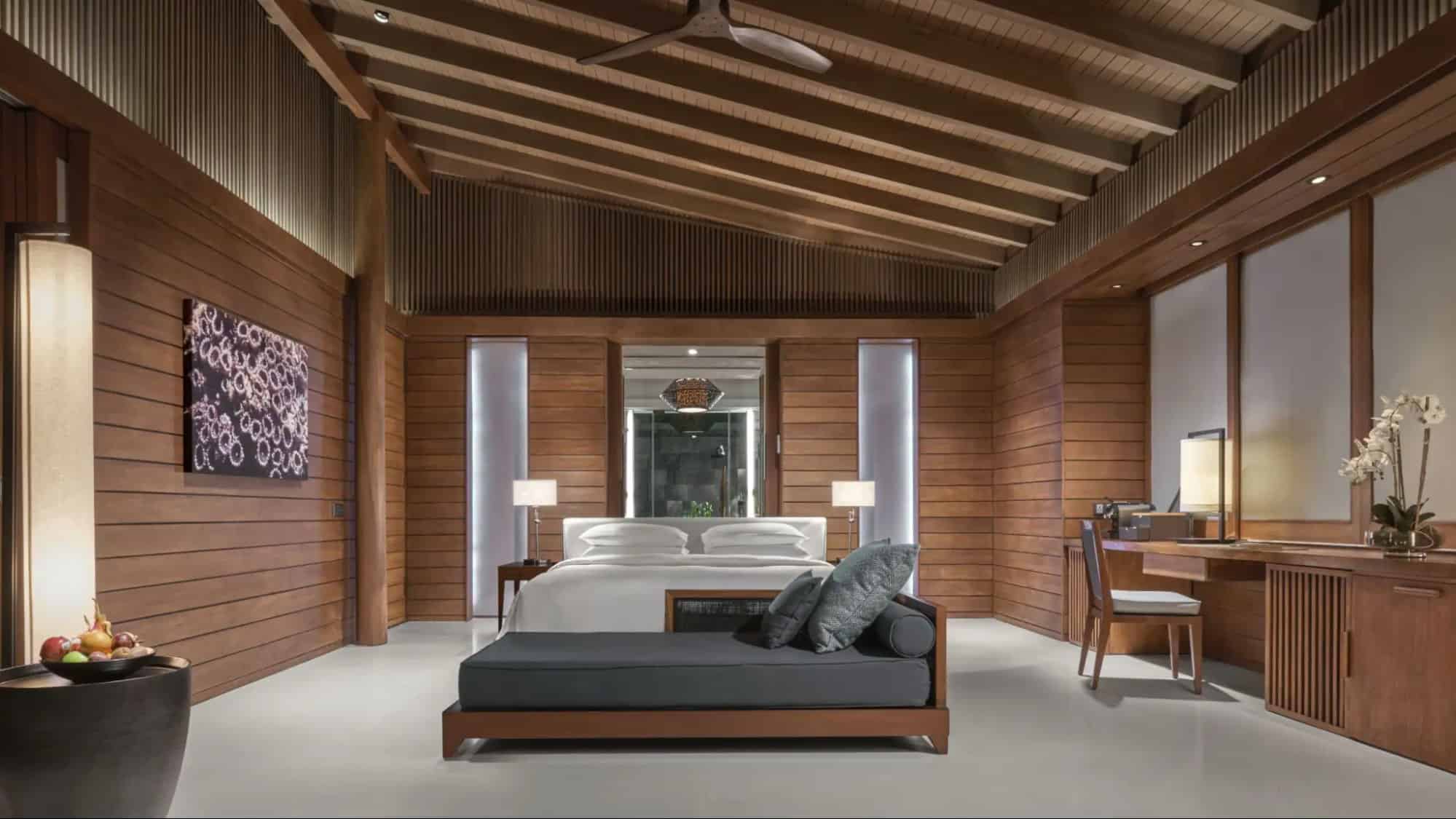 Spacious bedroom interior at Park Hyatt Maldives Hadahaa featuring wood-paneled walls, a king bed, vaulted ceiling, and modern luxury furnishings