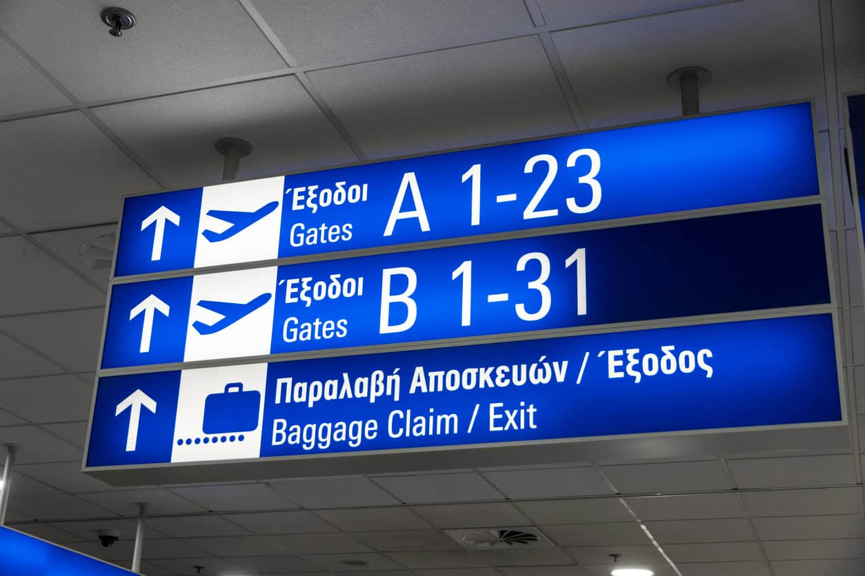 Airport direction sign showing gates A and B numbers with arrows and baggage claim exit symbols in terminal ceiling area