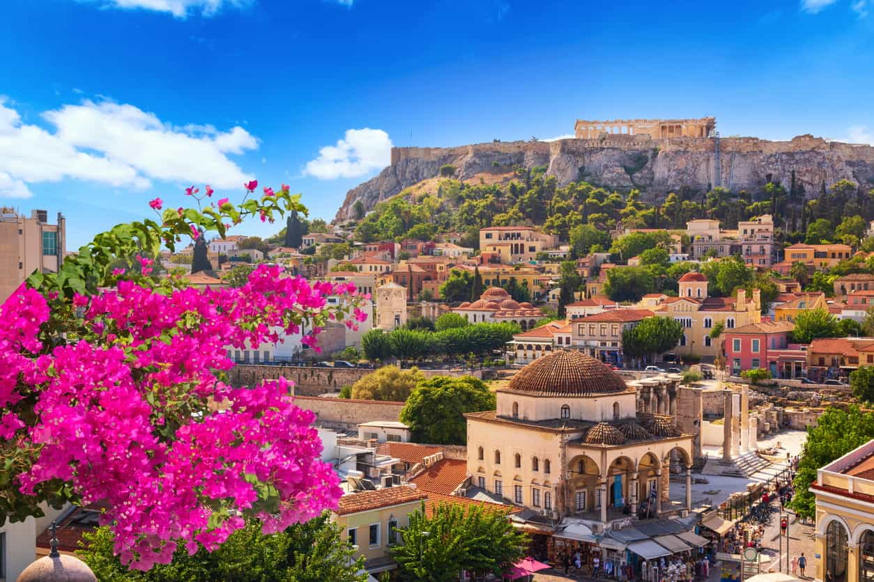 View of Athens with Acropolis hill above Monastiraki square, historic buildings and pink bougainvillea flowers in foreground under blue sky