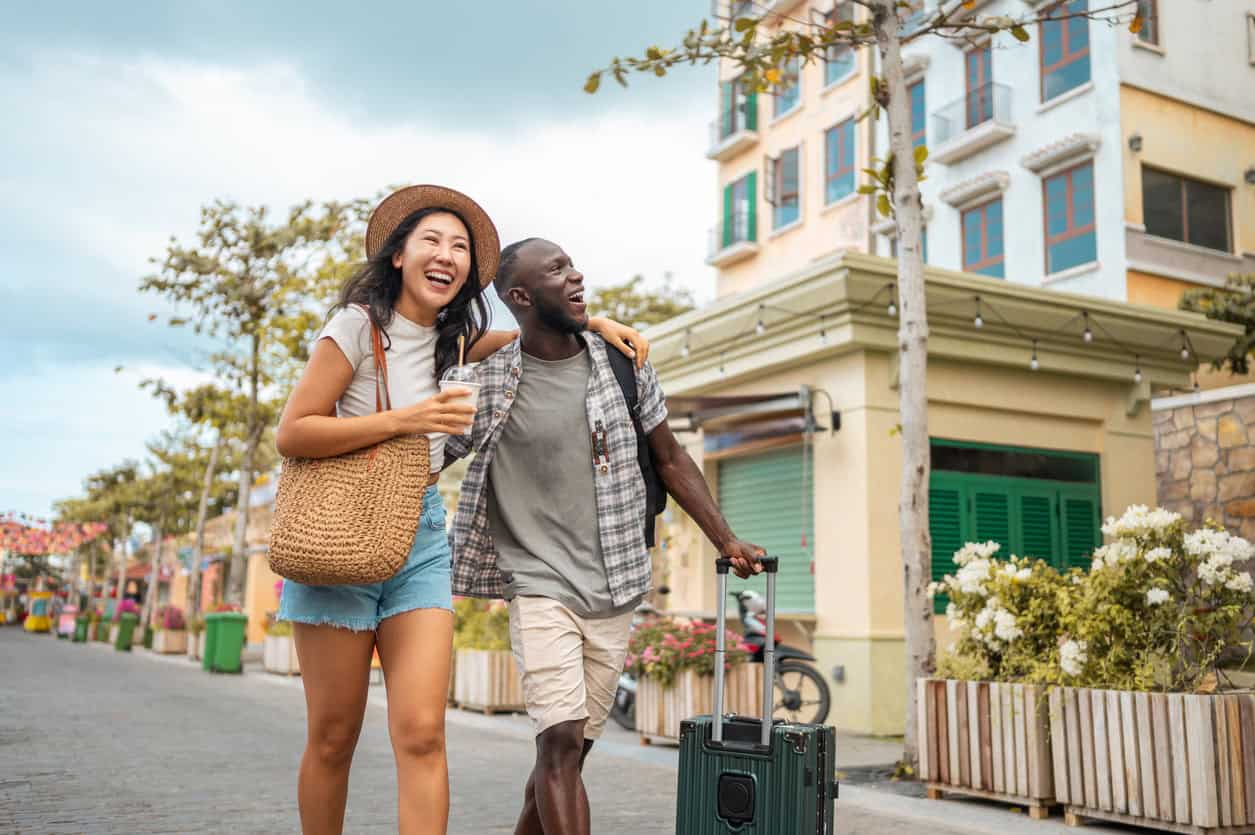 Happy couple walking through a colorful city street with luggage, enjoying their vacation together