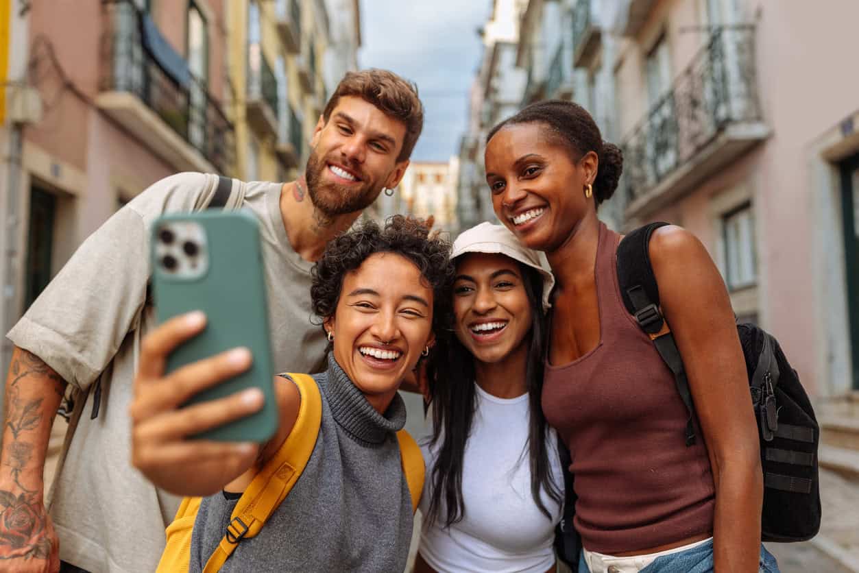 Group of friends taking a selfie while traveling in a city street, smiling with backpacks and urban buildings in the background