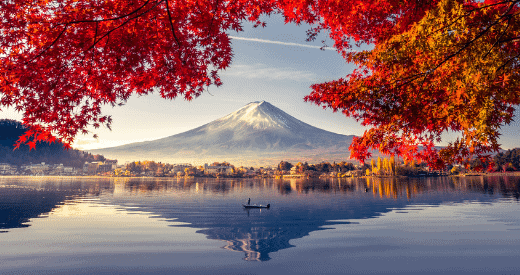 A lone boat floats on a calm lake, reflecting Mount Fuji in the background. Vibrant red autumn leaves frame the scene, as clear skies and soft sunlight make it a serene travel destination to earn miles or points.
