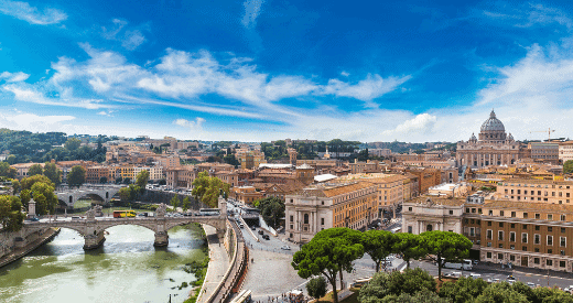 A panoramic view of Rome, Italy, featuring the Tiber River, historic bridges, and the dome of St. Peter’s Basilica beneath a bright blue sky with scattered clouds—a must-see for any travel enthusiast.