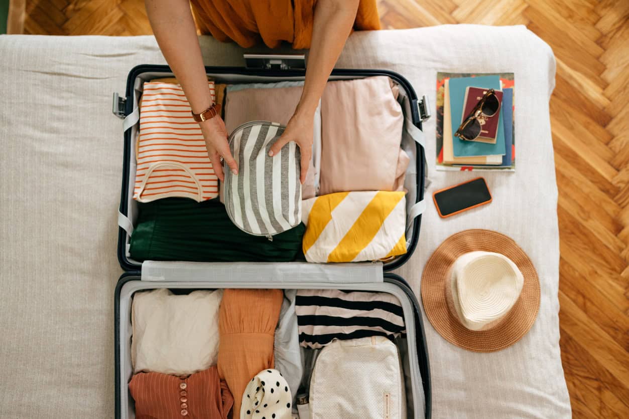 person organizing travel essentials and clothing in an open suitcase before a trip