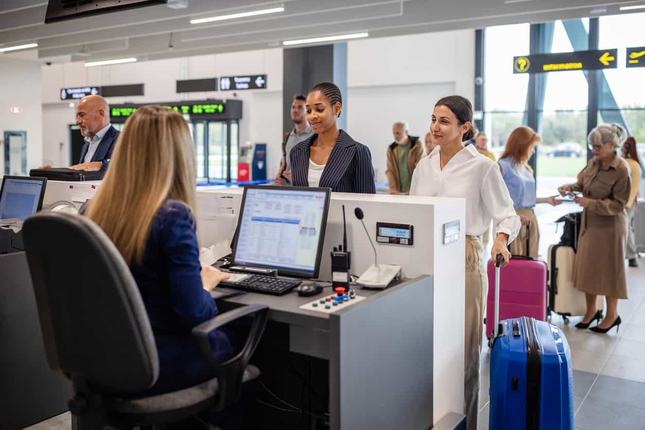 Travelers waiting in line at an airport check-in counter with rolling suitcases before a flight.