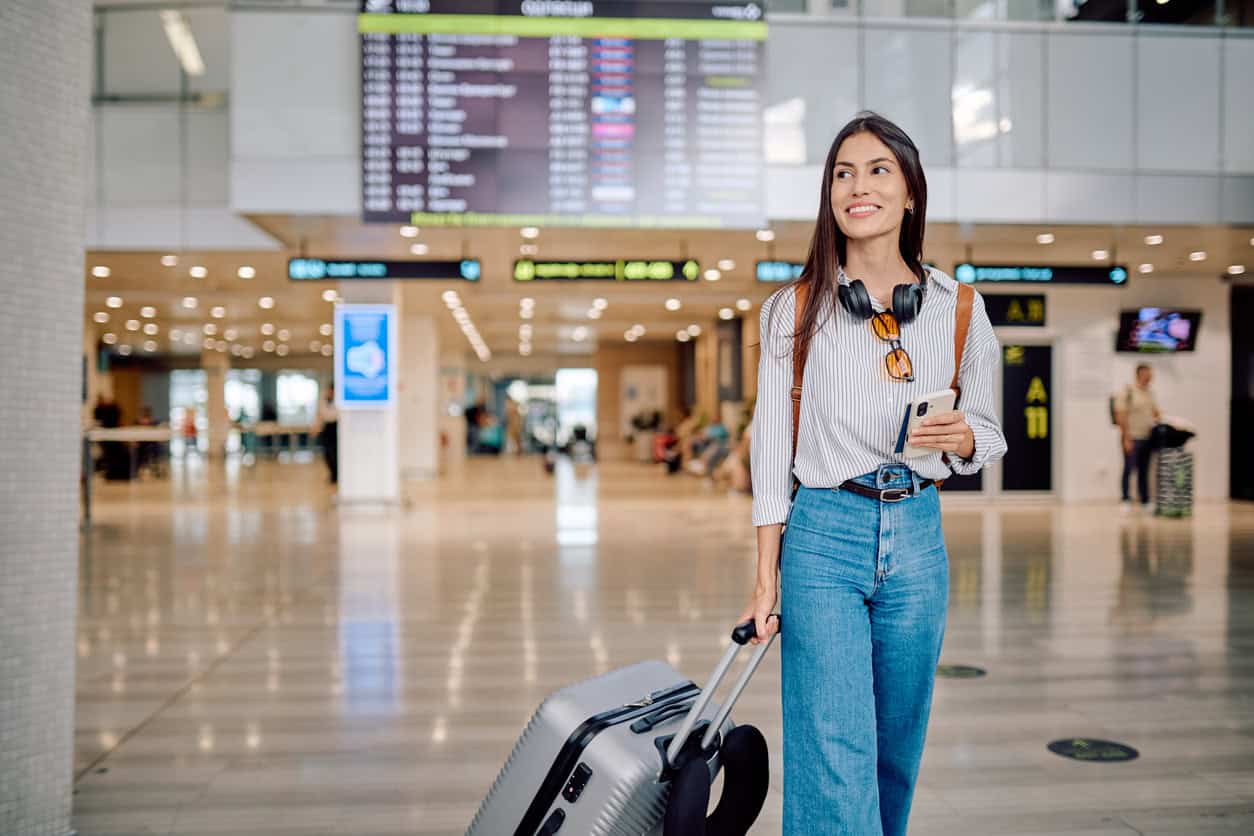 Solo traveler walking through an airport terminal with a rolling carry-on suitcase and smartphone.