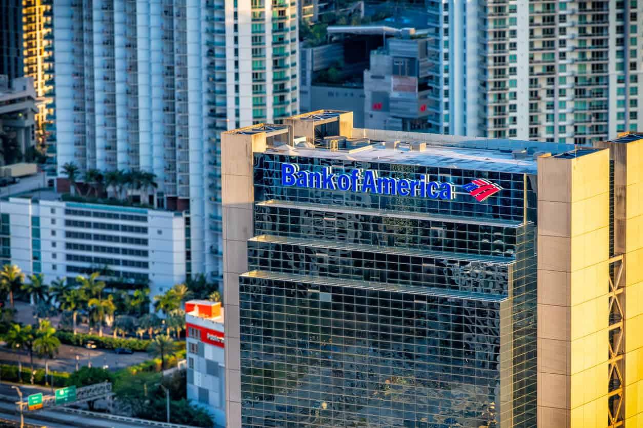 Bank of America logo on a glass office tower, with surrounding high-rise buildings and a city skyline in the background