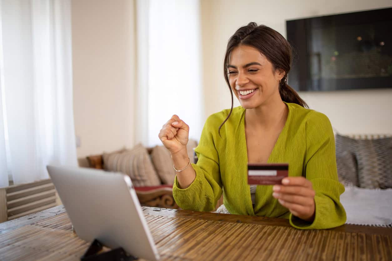 Smiling woman holding a credit card while shopping online on a laptop at home