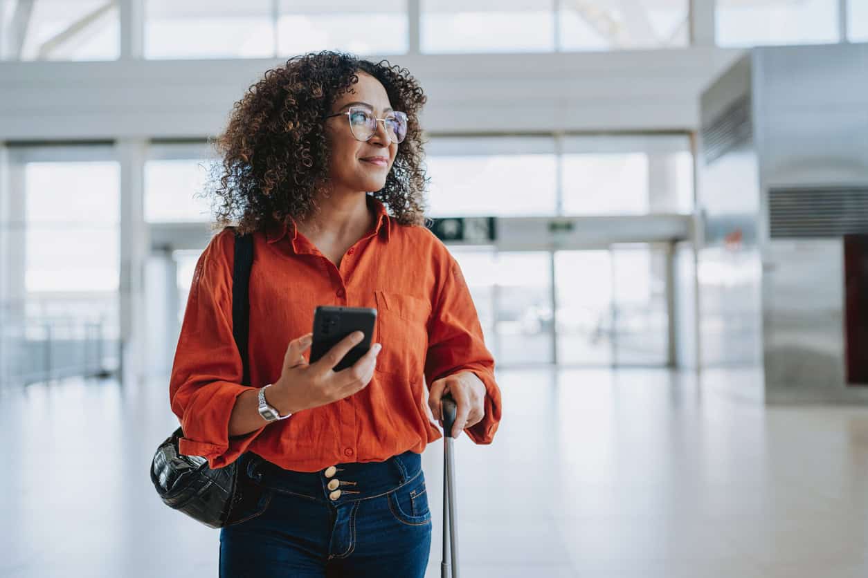 Traveler at the airport checking a mobile phone before departure, a common step when managing points and miles bookings or flight reservations.
