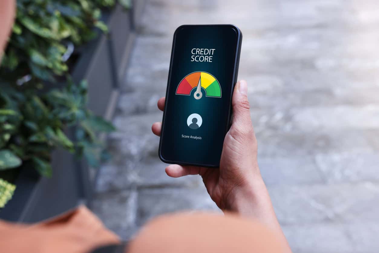 Person holding a smartphone displaying a credit score gauge on a mobile app