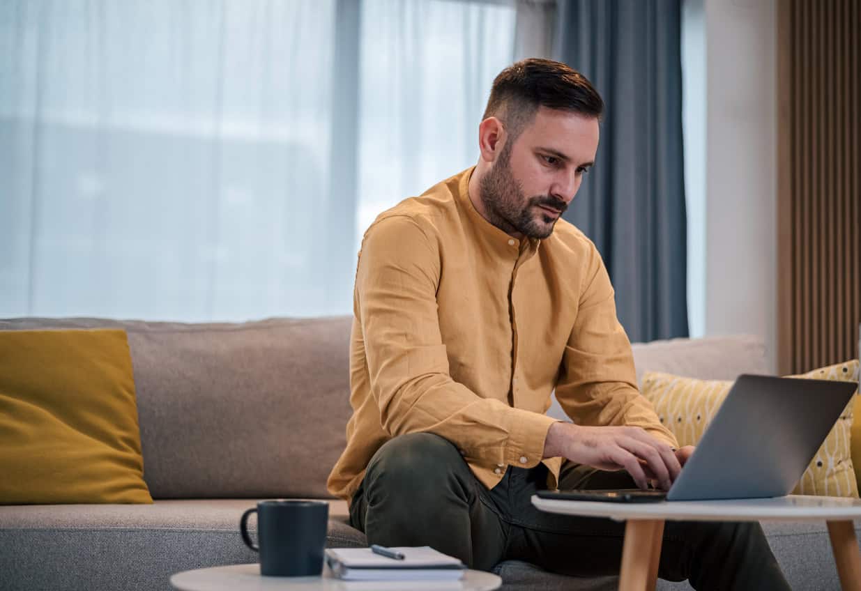Man working on a laptop at home while reviewing eligible Amex card and product options