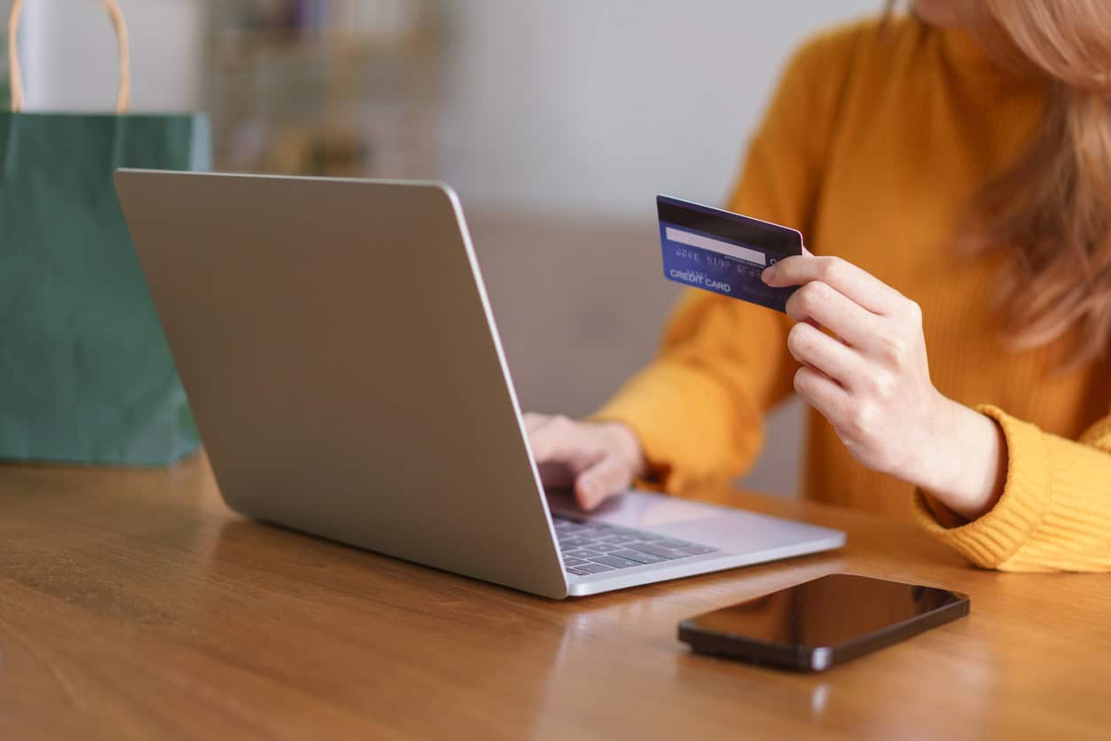 Person holding a credit card while shopping online on a laptop at a table
