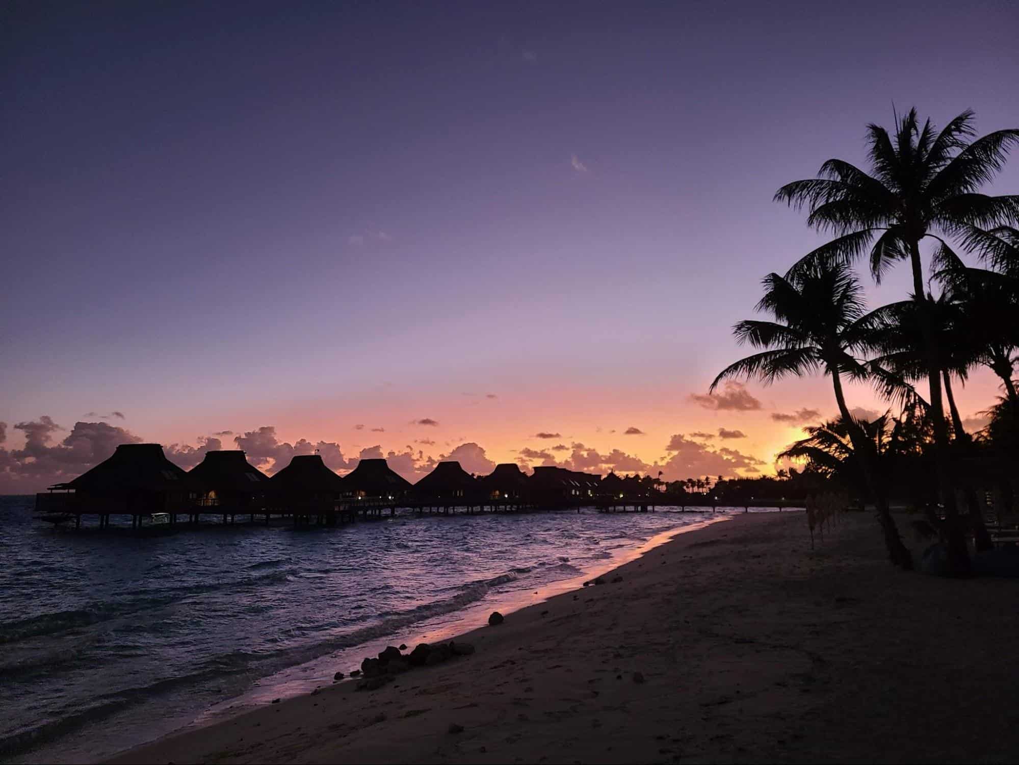 The sun sets behind the overwater bungalows at the Conrad Bora Bora Nui