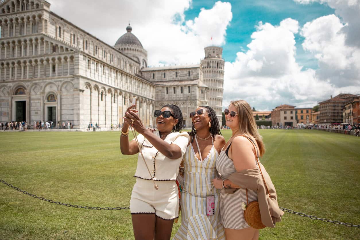 Three tourists taking a selfie in front of the Leaning Tower of Pisa in Italy.