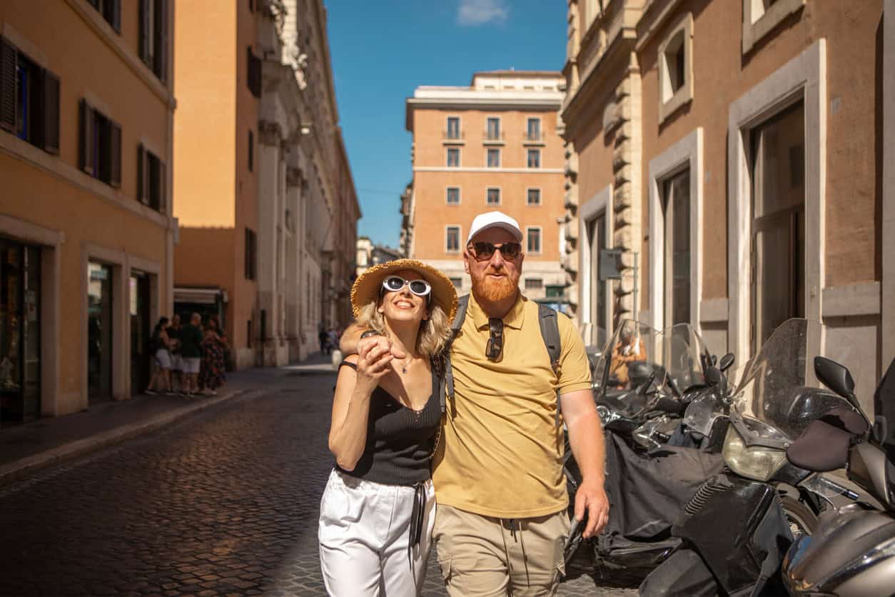 Tourists walking along a sunny cobblestone street in Rome, Italy, during a sightseeing trip.