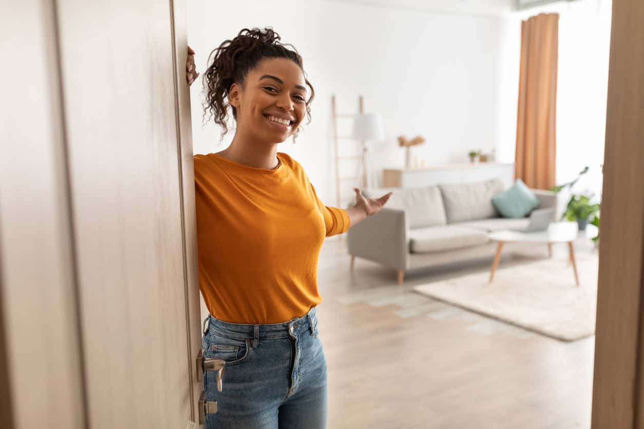 Smiling woman opening the door and welcoming someone into a bright modern living room