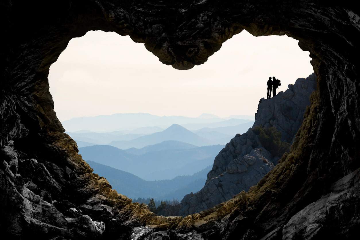 Heart shaped cave opening with a couple hiking