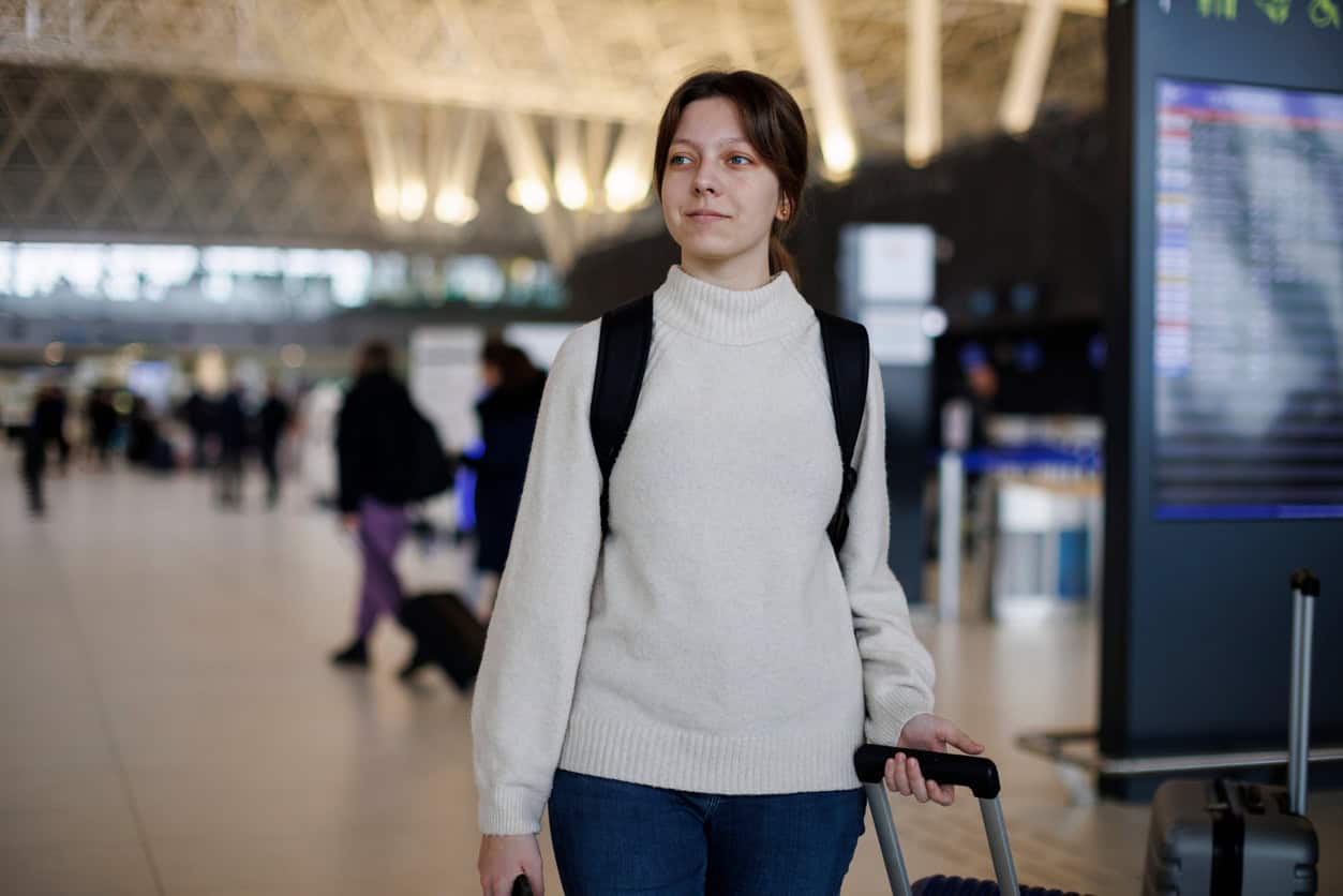 Young woman standing in an airport terminal with a suitcase and backpack, ready for travel.