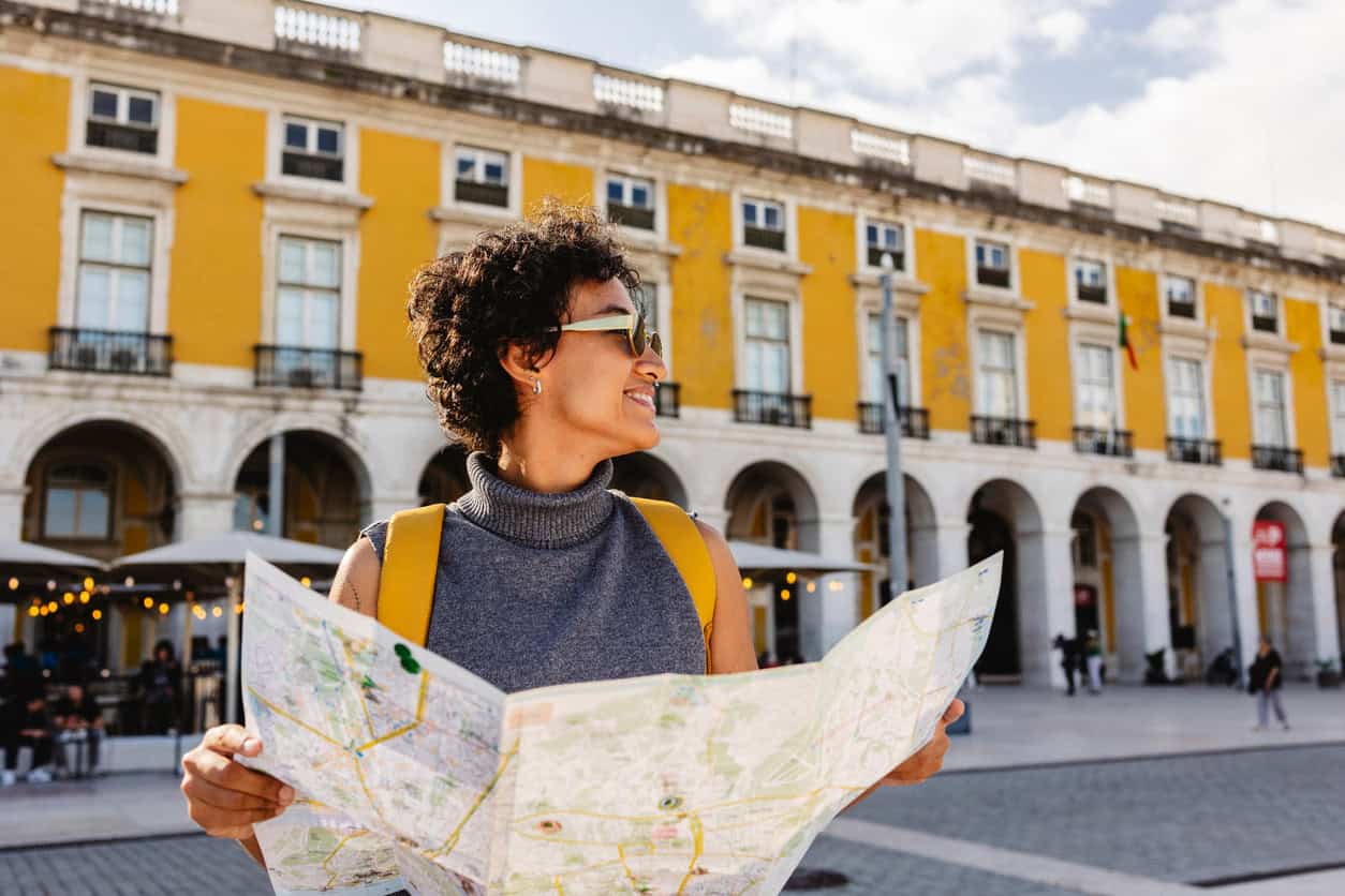 Smiling woman holding a city map while sightseeing in a historic yellow building plaza.