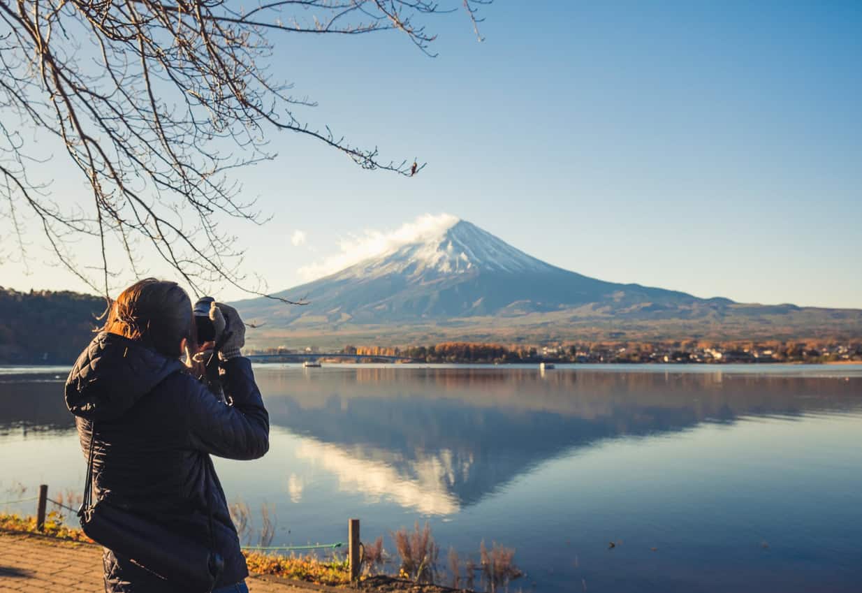 Tourist taking a photo of Mount Fuji reflected on a calm lake in Japan during a clear day