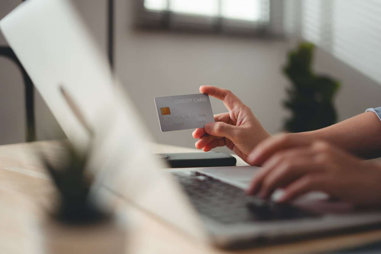 Person holding a credit card while typing on a laptop to make an online business purchase