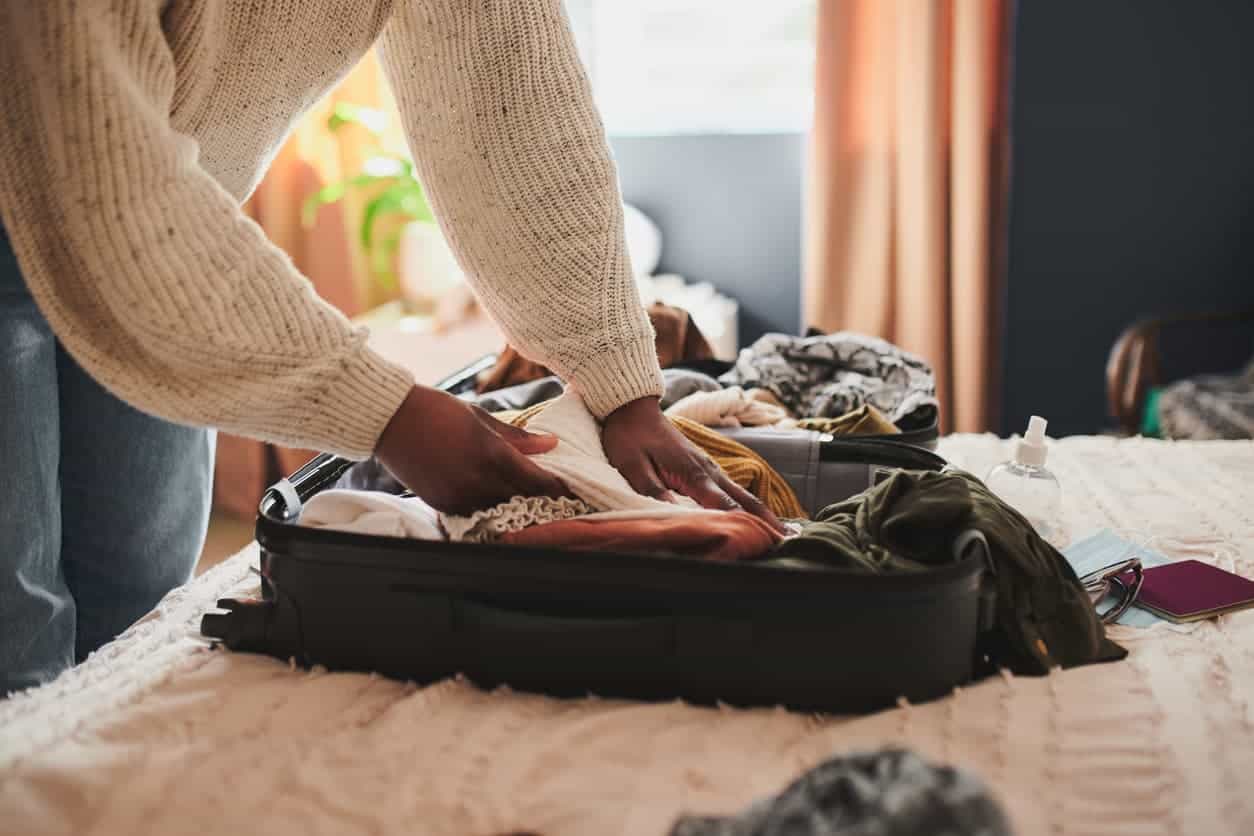 Person packing clothes into a suitcase on a bed before traveling