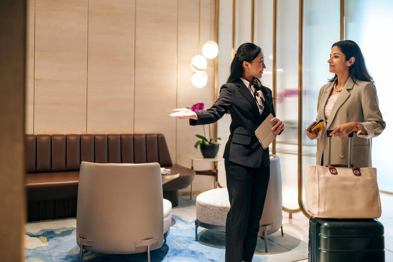 Business traveler arriving at an airport lounge and being welcomed by staff with luggage