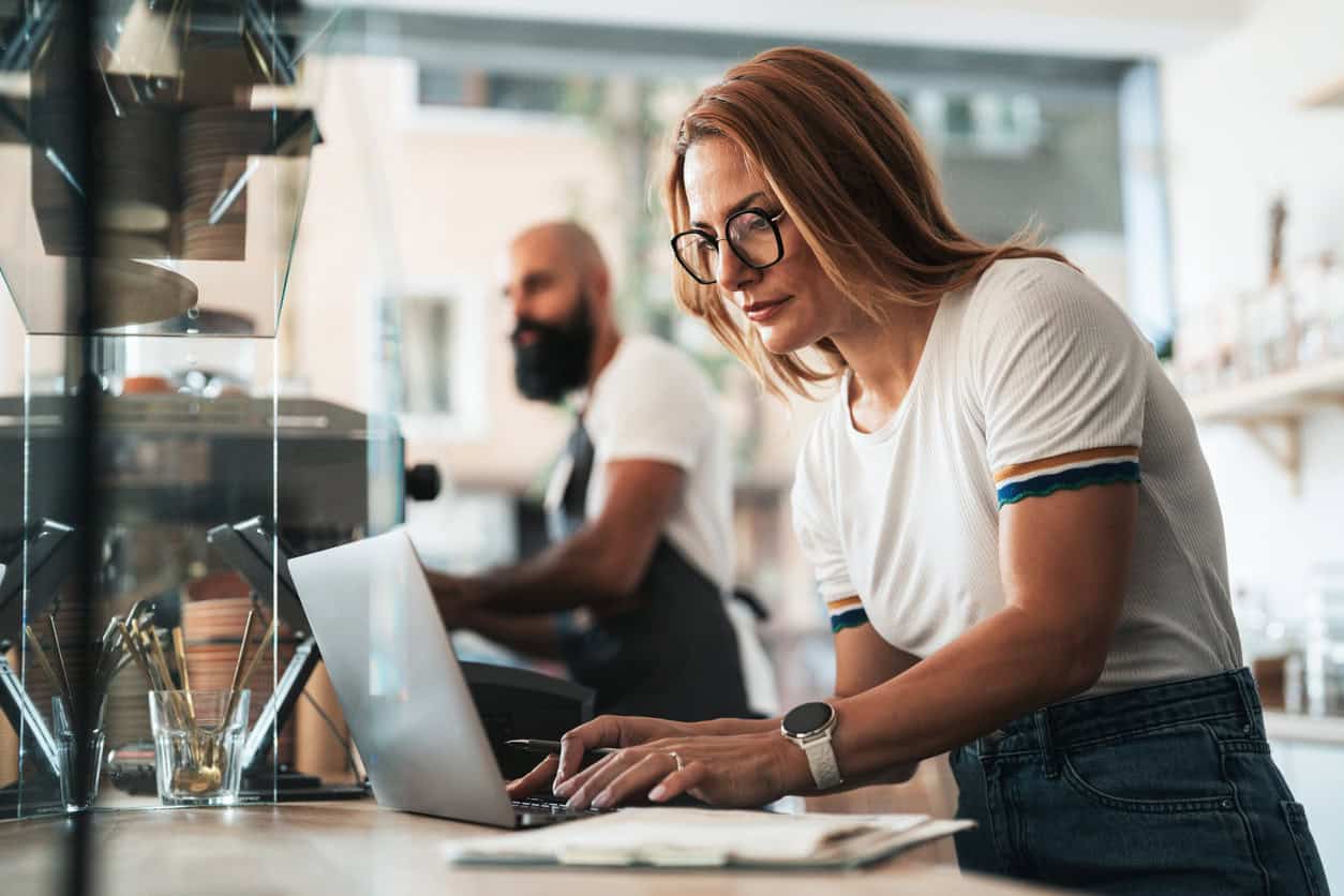 Small business owner working on a laptop at a café counter while managing daily operations