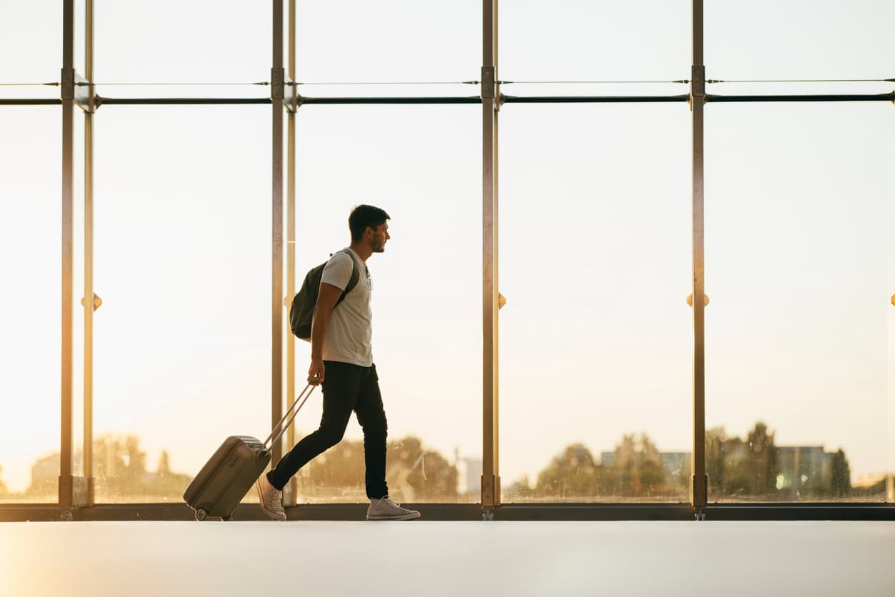 A man walking through an airport terminal pulling a suitcase.