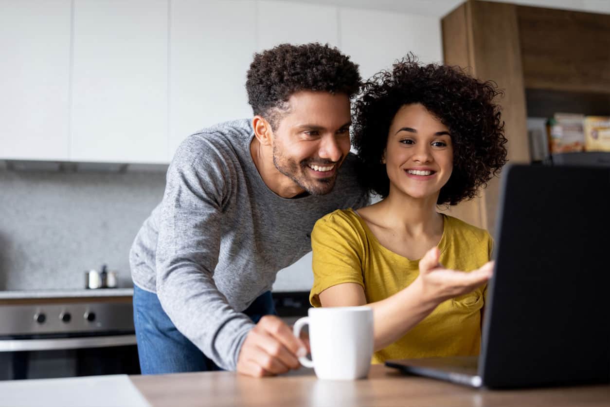 Couple reviewing and discussing travel options on an online booking portal using a laptop at home