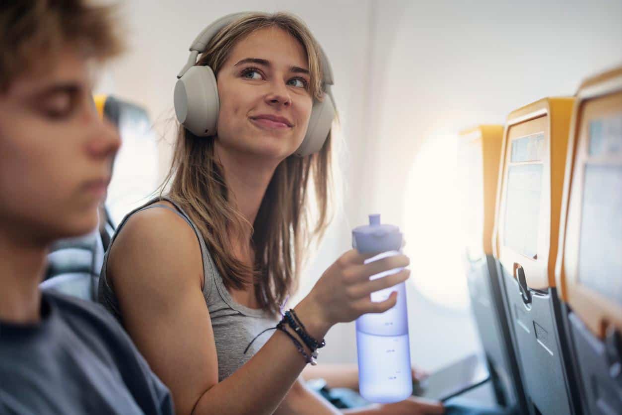 Young woman wearing headphones and holding a water bottle while seated on an airplane