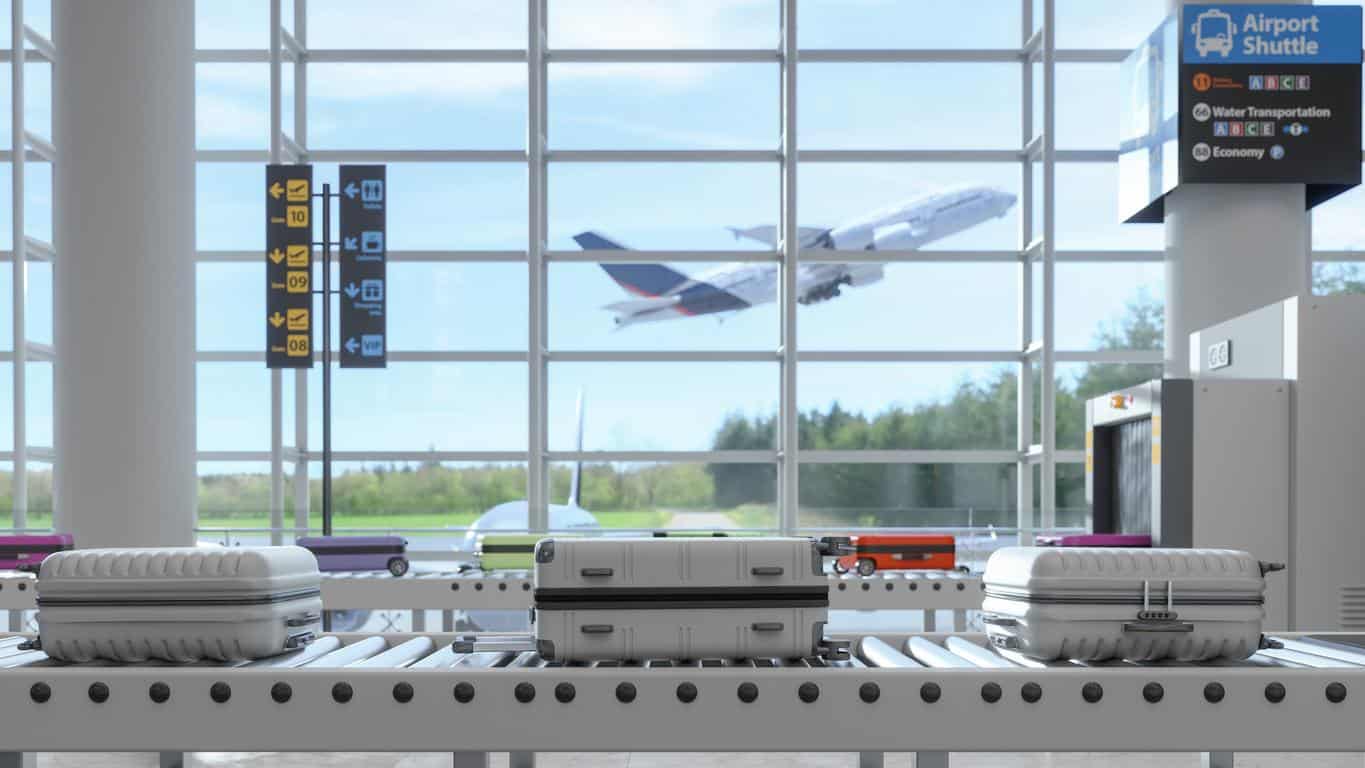 Luggage on airport conveyor belt with airplane taking off in the background through large glass windows
