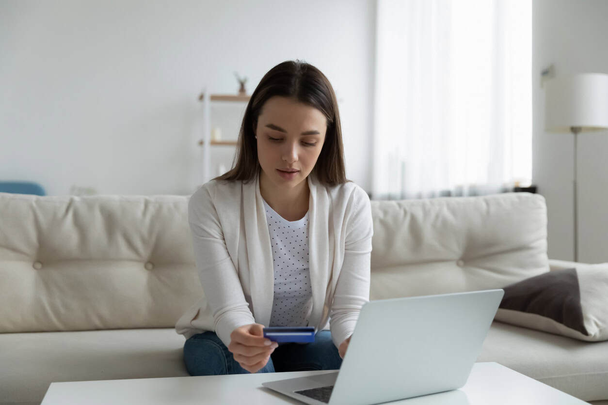 Woman reviewing updated credit card eligibility rules on her laptop while holding her card at home.