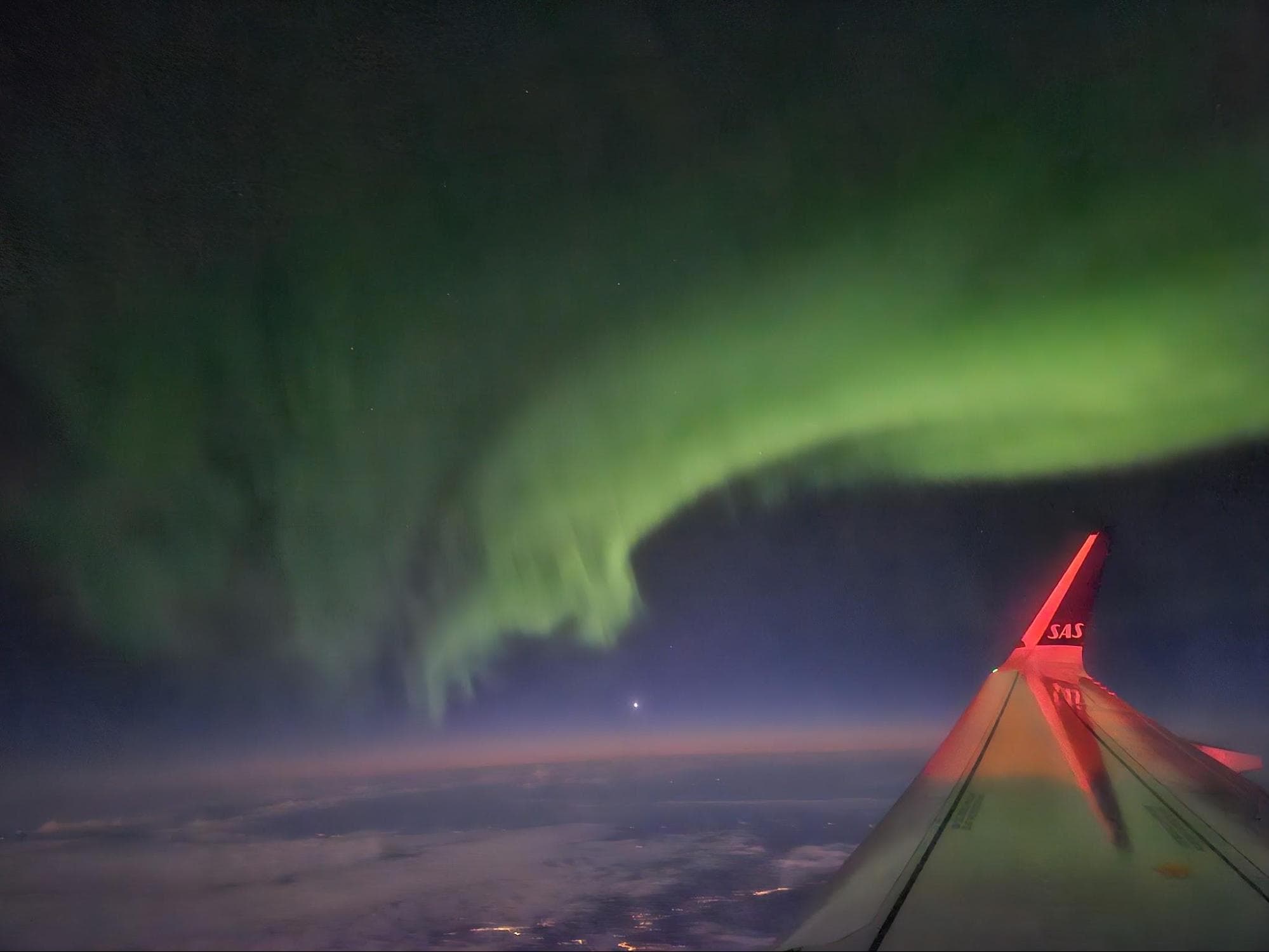 View of the northern lights from an SAS airplane window while flying over between Tromsø and Oslo.