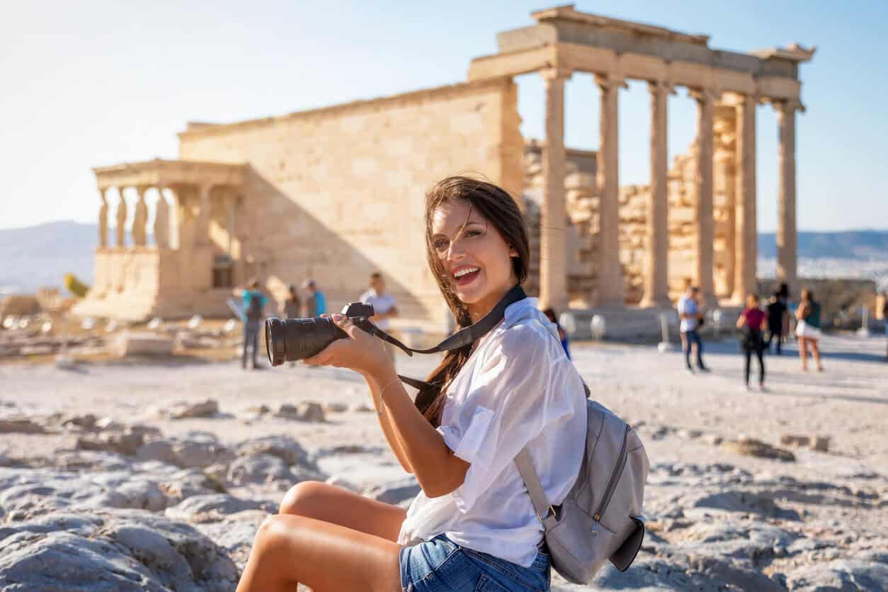 Female tourist holding a camera with ancient Greek ruins in the background at the Acropolis in Athens