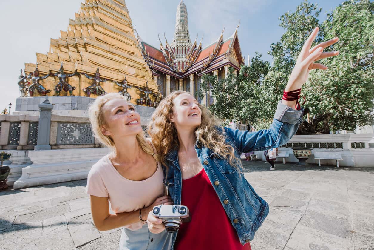 Two female tourists smiling and pointing while exploring the Grand Palace in Bangkok, Thailand