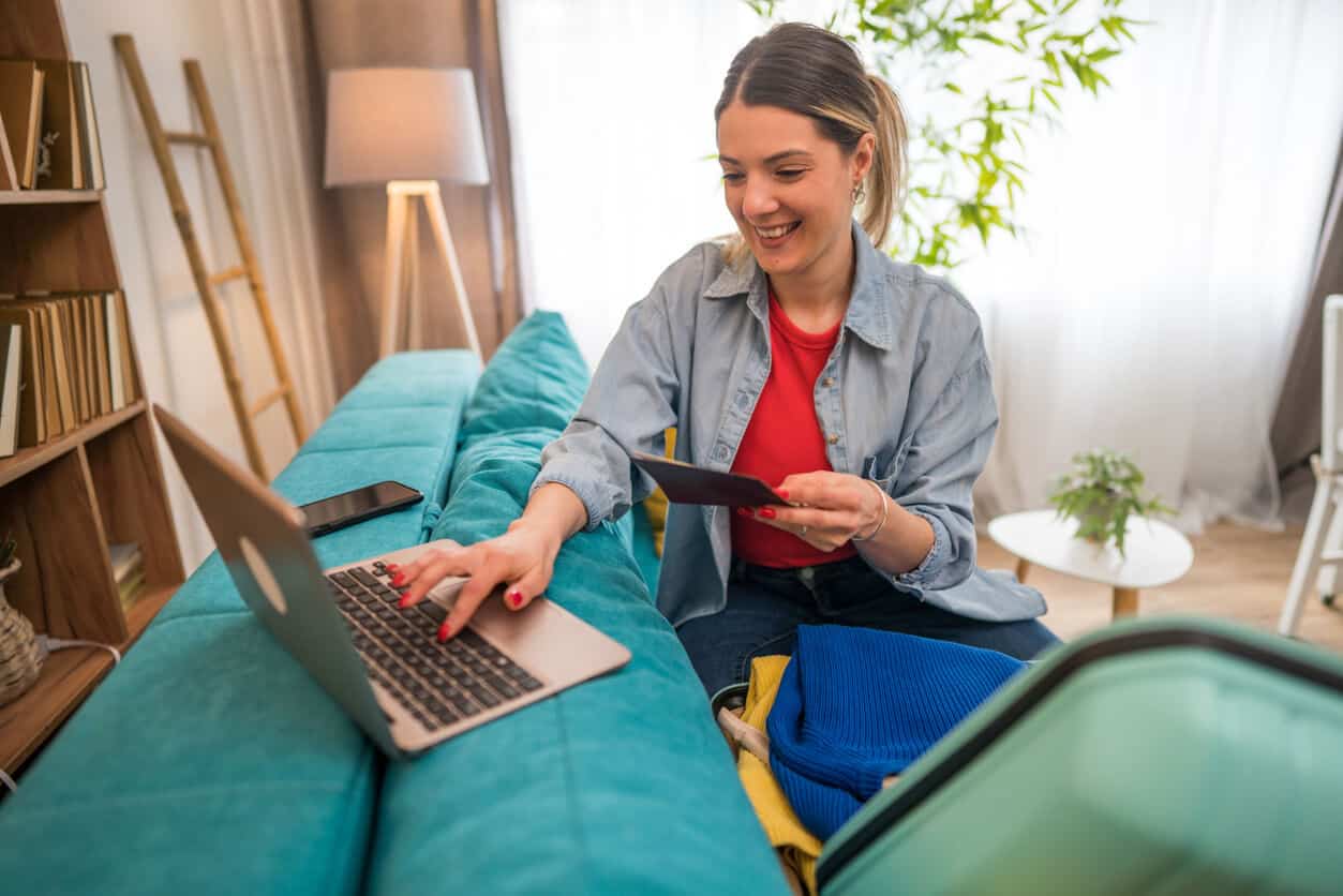 Woman holding a passport while booking a trip on her laptop at home