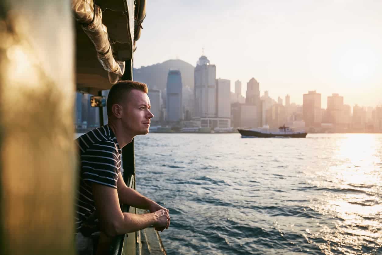 Man enjoying a scenic sunset view of Hong Kong’s skyline from a ferry on Victoria Harbour.